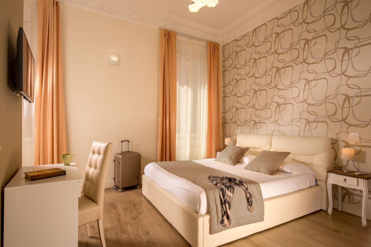 A hotel room with a bed, a desk, a chair, a suitcase, and a television.