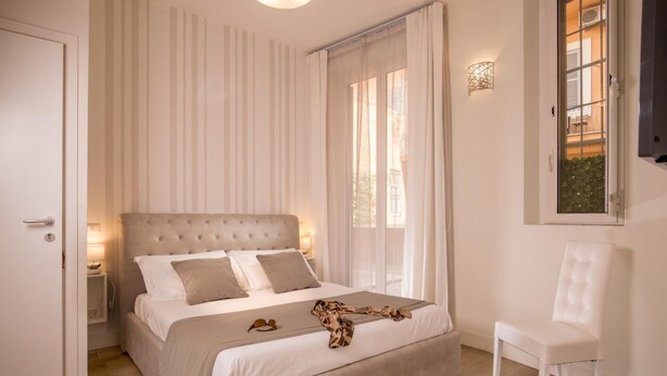 A bedroom with a large bed, a chair, a nightstand, and a window with curtains. - Royal Rooms Corso (Rome)