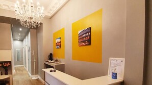 A reception desk with a chandelier, a framed certificate, and two framed pictures on the wall. - Royal Rooms Corso (Rome)