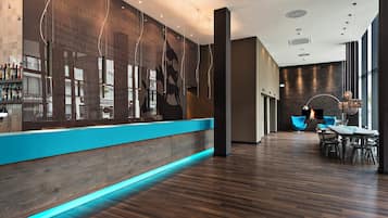 Un moderno vestíbulo de hotel con mostrador de recepción de madera, chimenea y zona de estar con sillas azules.