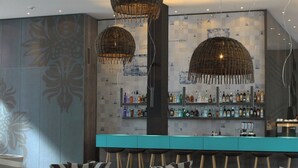 Una zona de bar con mostrador color turquesa, taburetes de madera y lámparas de mimbre colgantes.