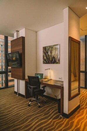 Una habitación de hotel con escritorio, silla, televisión y un cuadro.