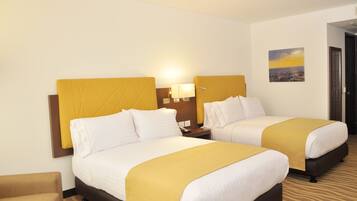 A hotel room with two beds, a nightstand with a lamp, a chair, and a painting on the wall.