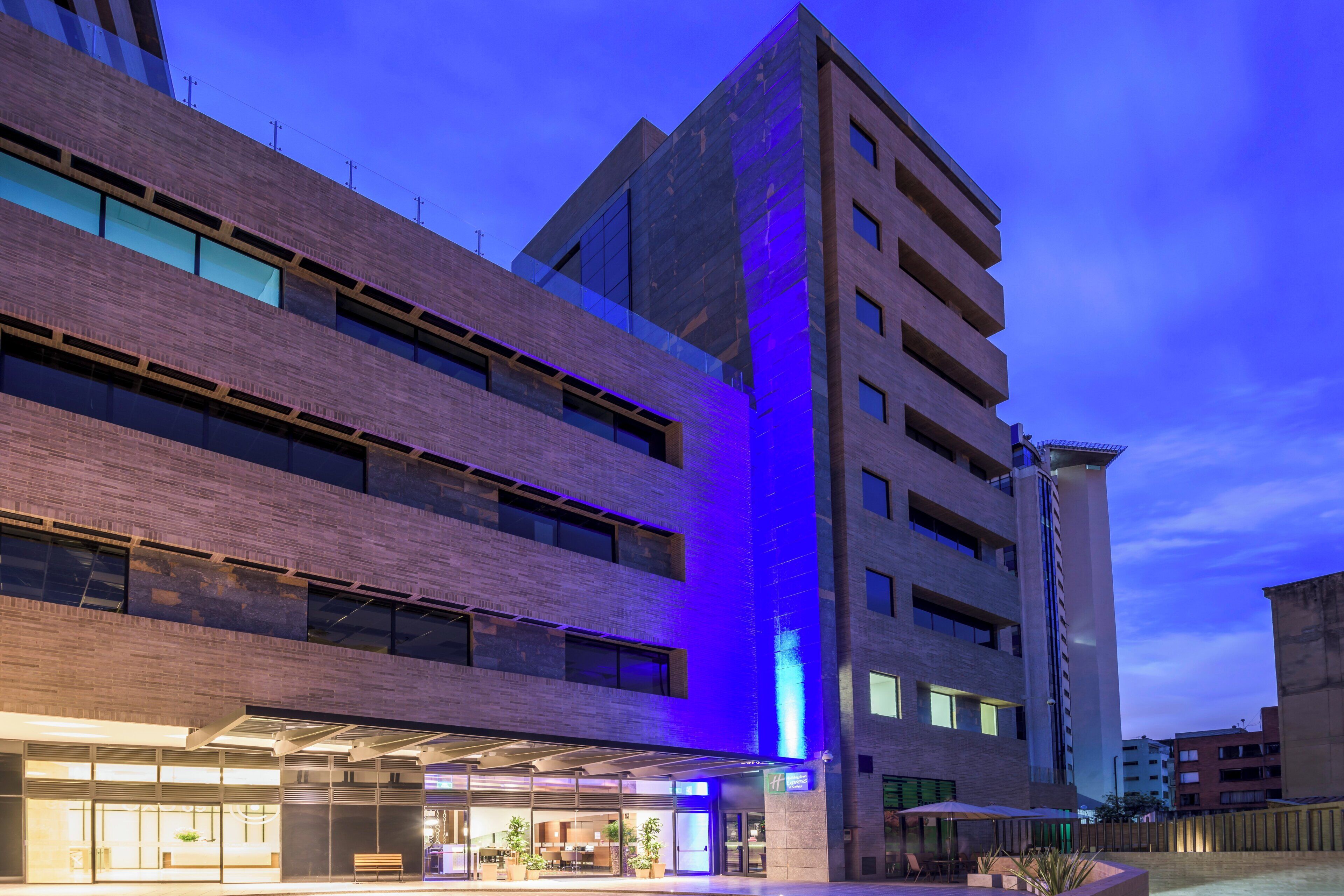 Un hotel de varios pisos con diseño moderno, que presenta una llamativa estructura vertical iluminada en la fachada.