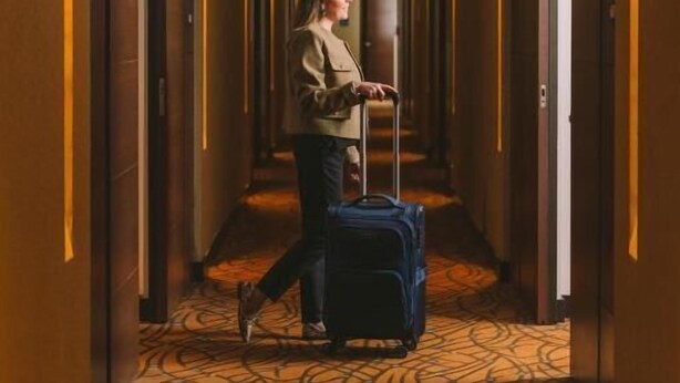 A hotel corridor with a patterned carpet, a person with a suitcase, and a door at the end. - Holiday Inn Express & Suites Bogota DC (Bogotá)