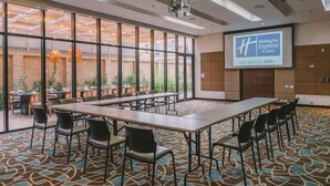 A conference room with a large screen displaying the Holiday Inn Express & Suites logo, a long table with chairs, and a view of the outdoor patio area. - Holiday Inn Express & Suites Bogota DC (Bogotá)