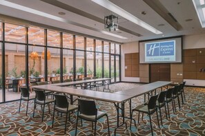 Un salón de conferencias con una pantalla grande mostrando el logotipo de Holiday Inn Express & Suites, una mesa larga con sillas y vistas al área del patio exterior.