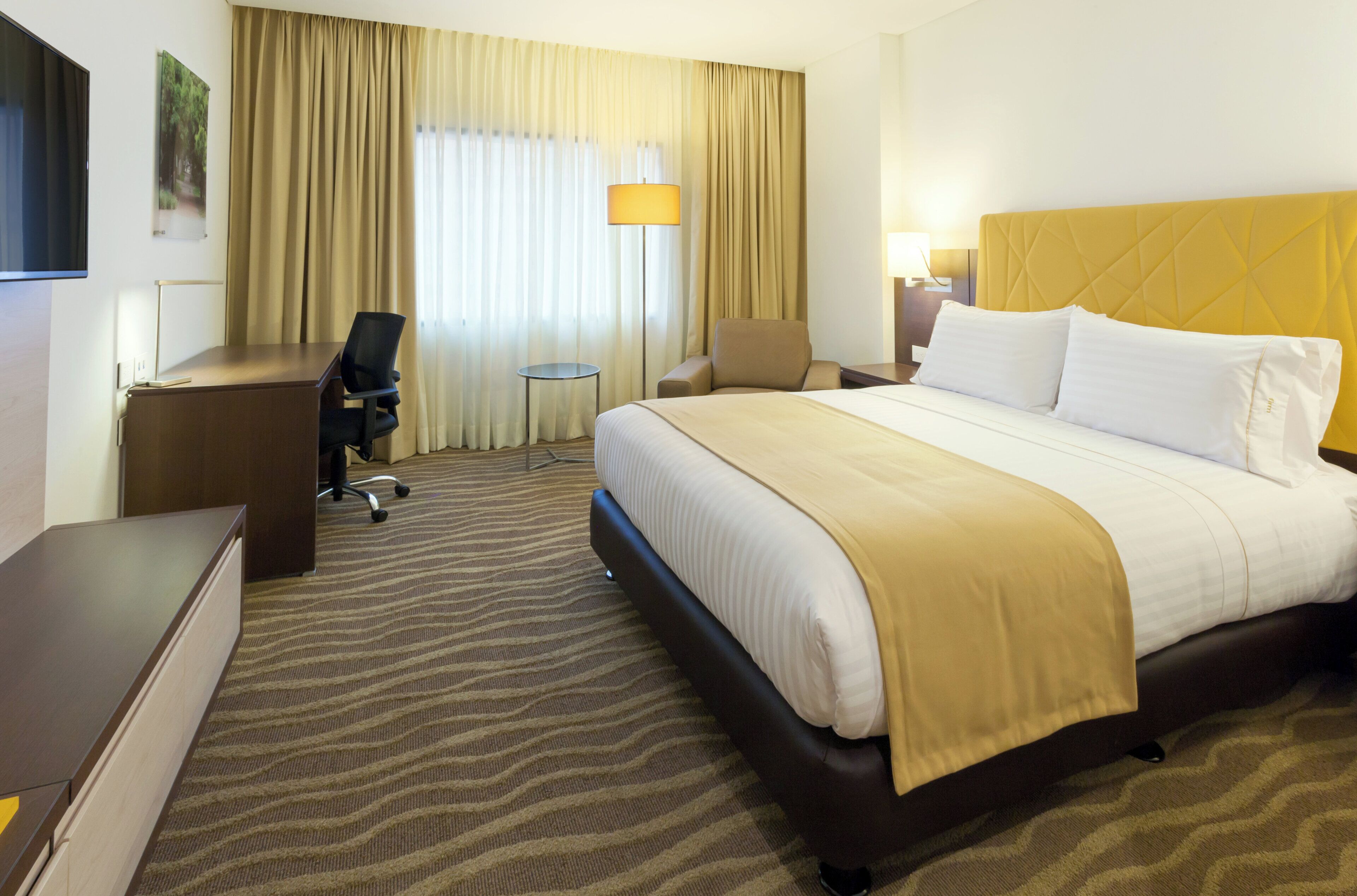 A hotel room with a bed, desk, chair, and a small table.