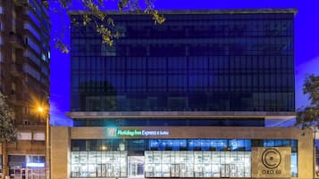 A Holiday Inn Express & Suites building with a modern glass facade, located at an urban intersection.