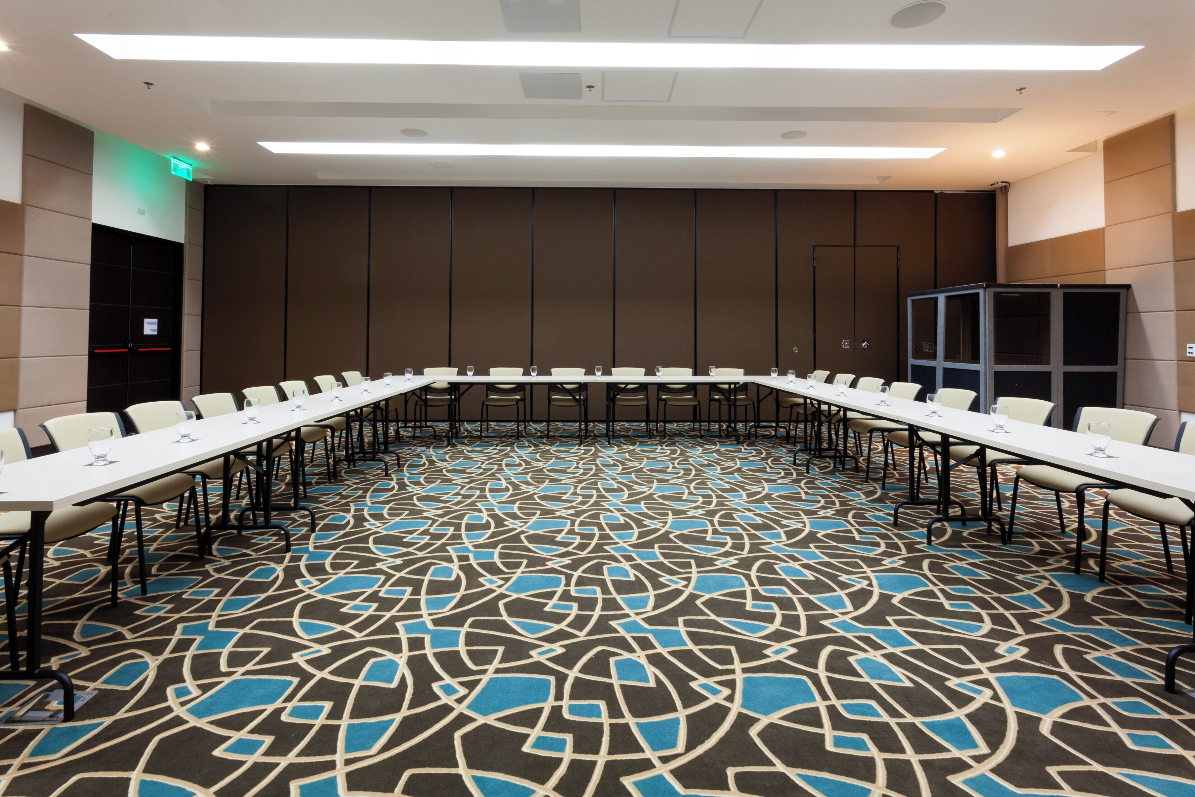 Un salón de conferencias con una mesa larga, sillas y una alfombra estampada.
