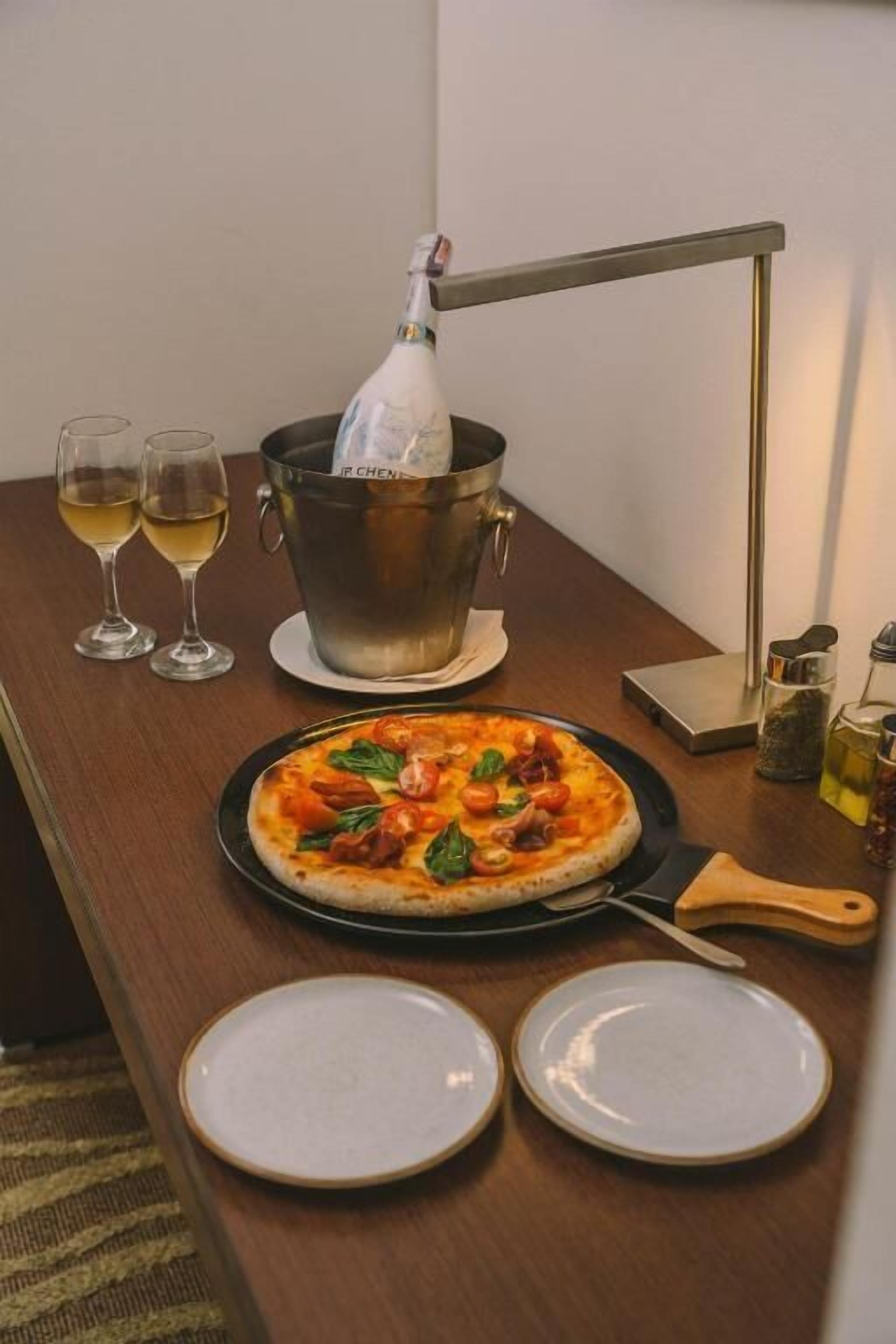 Een eettafel met pizza, twee glazen witte wijn, een champagnefles en een metalen emmer.