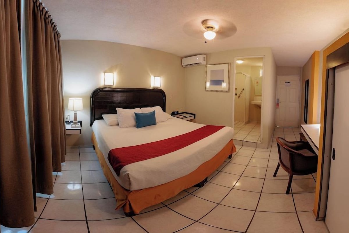 A hotel room with a large bed, a desk, and a chair.