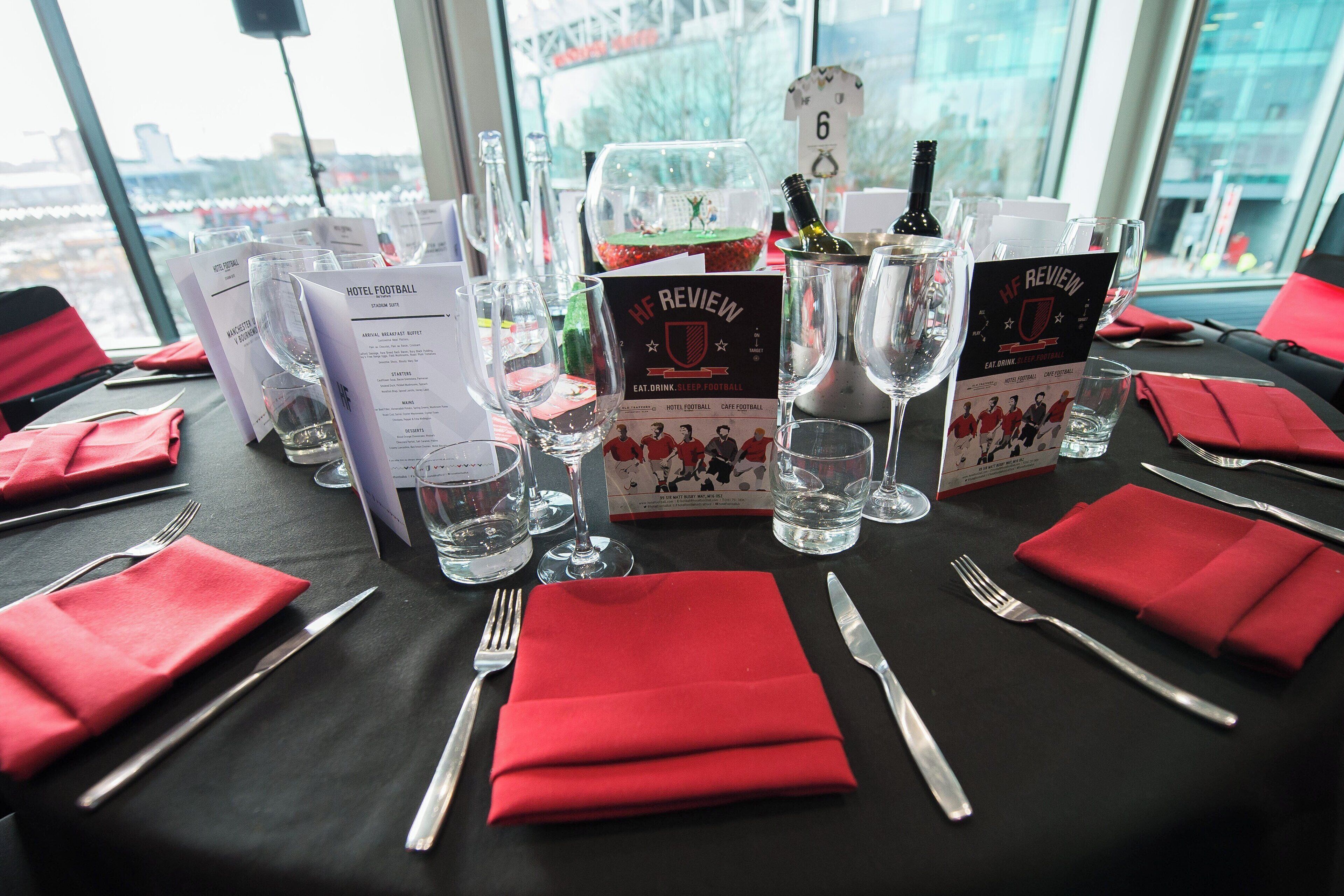 A hotel table set with red napkins, cutlery, and glasses, with menus and a bottle of champagne.