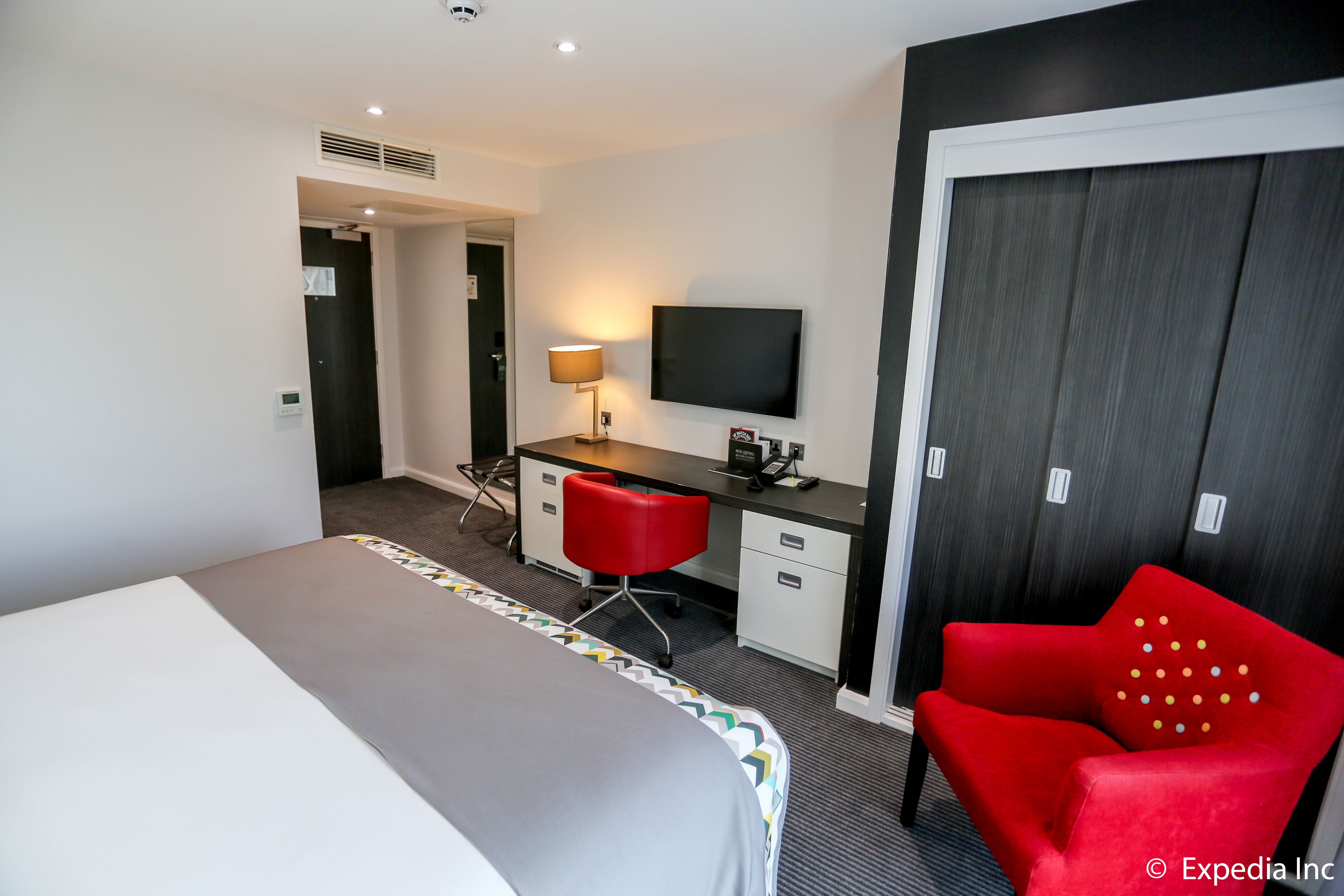 Hotelkamer met een bed, bureau, rode stoel, televisie en garderobe.
