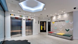 A modern hotel lobby with a hexagonal skylight, two elevators, a reception desk, and a wall with a 'Hotel Football' sign. - Hotel Football, Old Trafford, a Tribute Portfolio Hotel (Manchester)