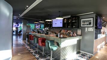 A modern bar area with a counter, stools, and a television screen.