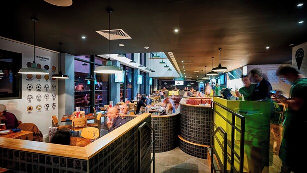 A modern restaurant interior with high ceilings, pendant lighting, and a central counter. - Hotel Football, Old Trafford, a Tribute Portfolio Hotel (Manchester)