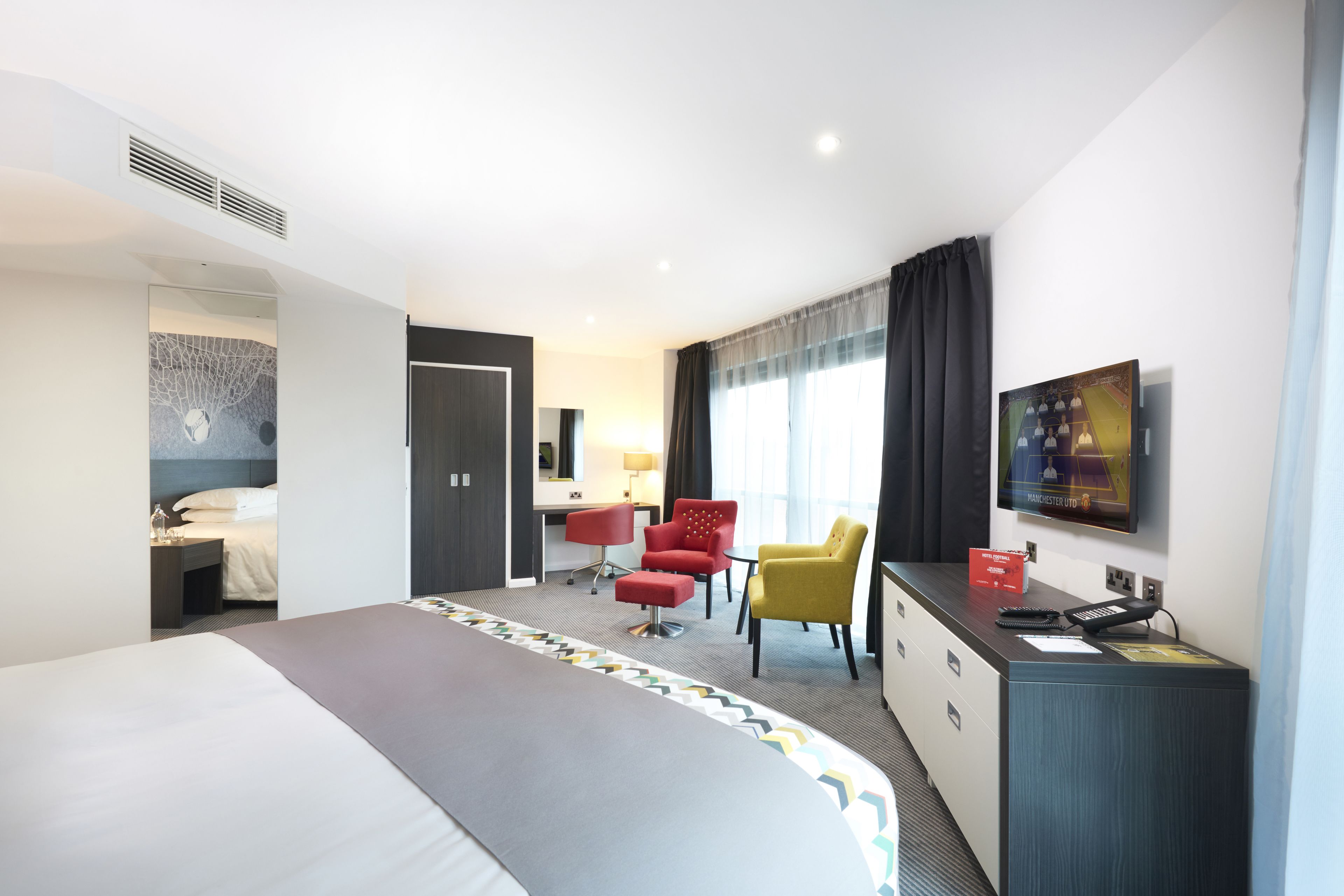 Una camera d'albergo con un letto grande, una scrivania con una sedia, una TV e un minibar.