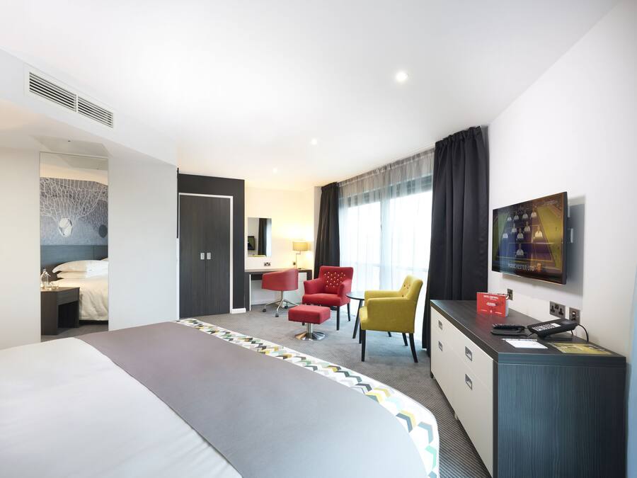Una camera d'albergo con un letto grande, una scrivania con una sedia, una TV e un minibar.
