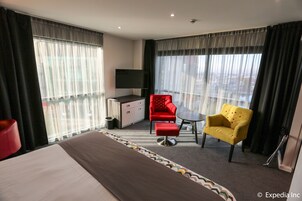 Una habitación de hotel con una cama, un sillón rojo, un sillón amarillo, una mesita y un televisor.