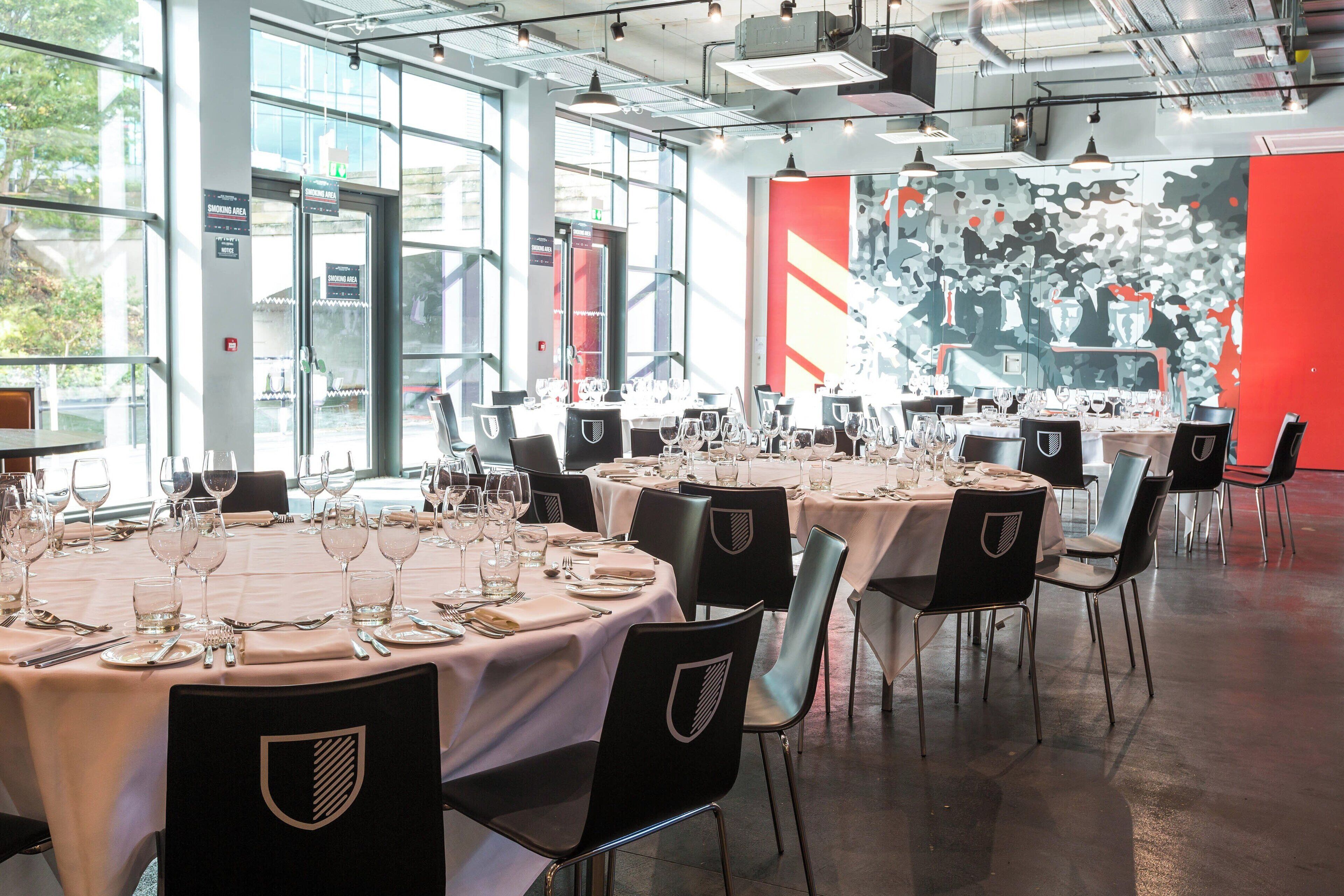 Un restaurant avec des tables rondes dressées pour le repas, chacune étant recouverte d’une nappe blanche et entourée de chaises noires.