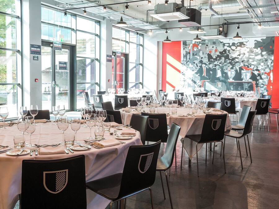 Un restaurant avec des tables rondes dressées pour le repas, chacune étant recouverte d’une nappe blanche et entourée de chaises noires.