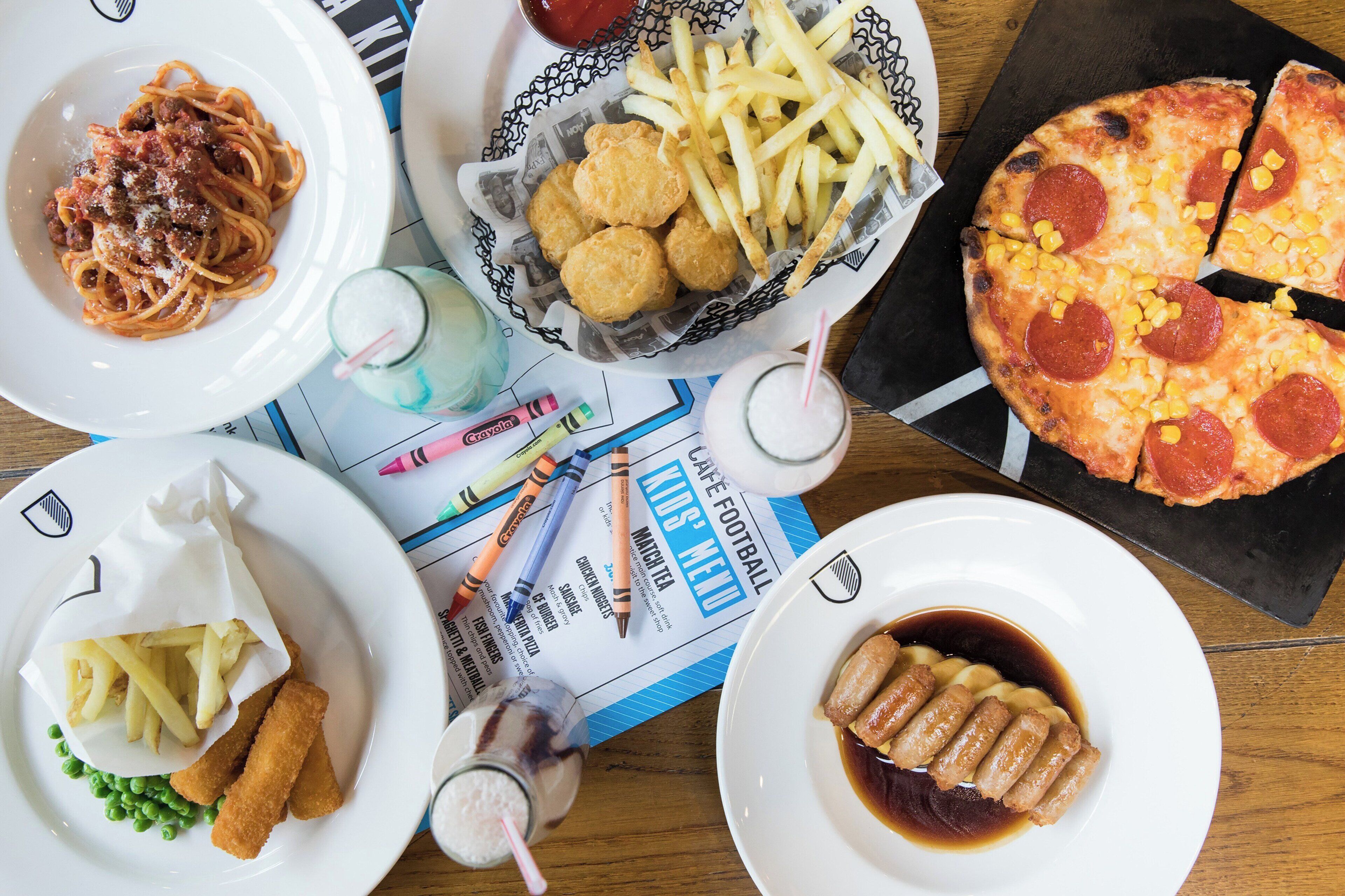 Uma mesa com vários pratos, incluindo espaguete, batatas fritas, pizza e salsichas.