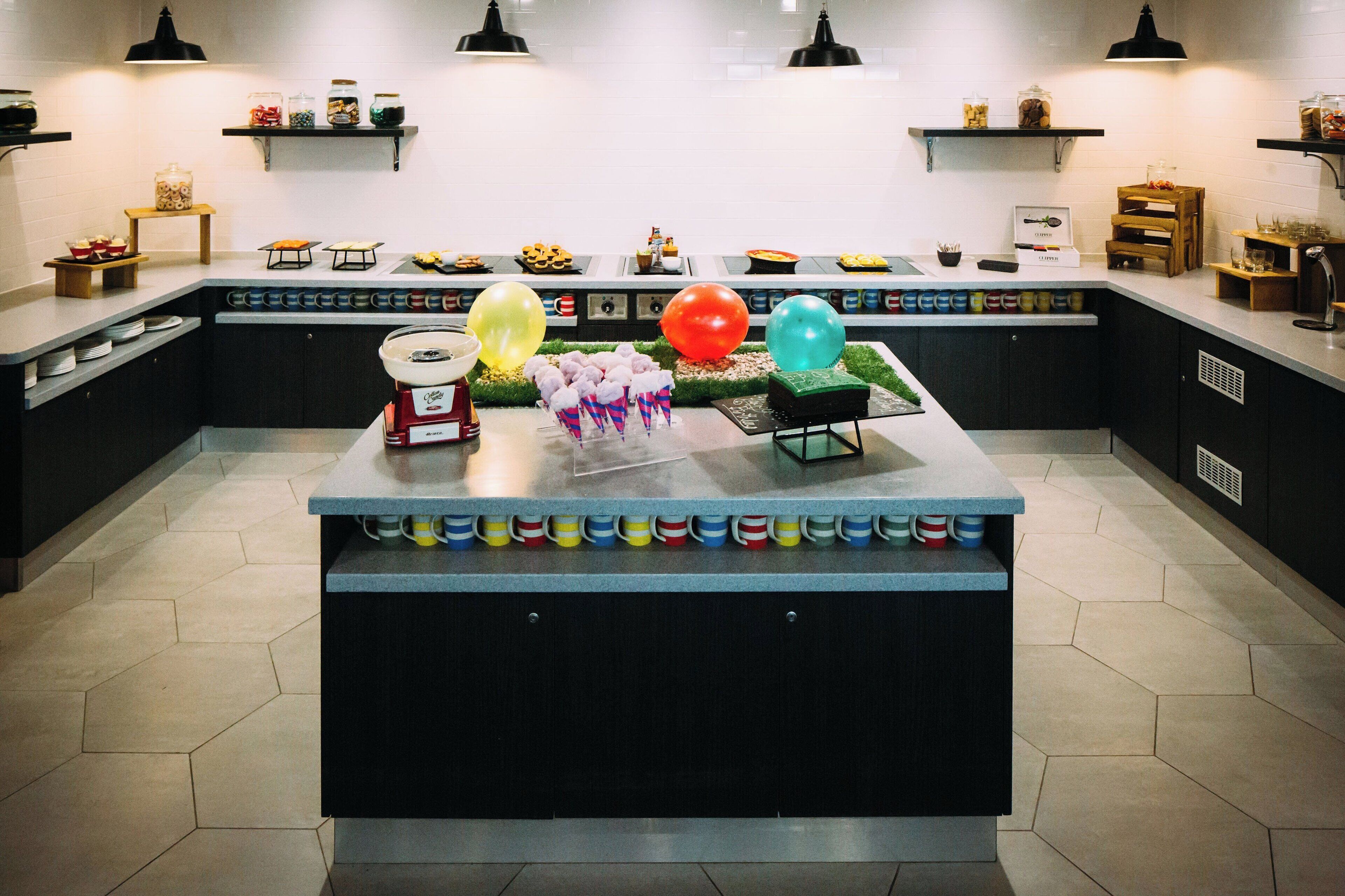 A kitchen with a central island, shelves with jars, and a variety of food items.