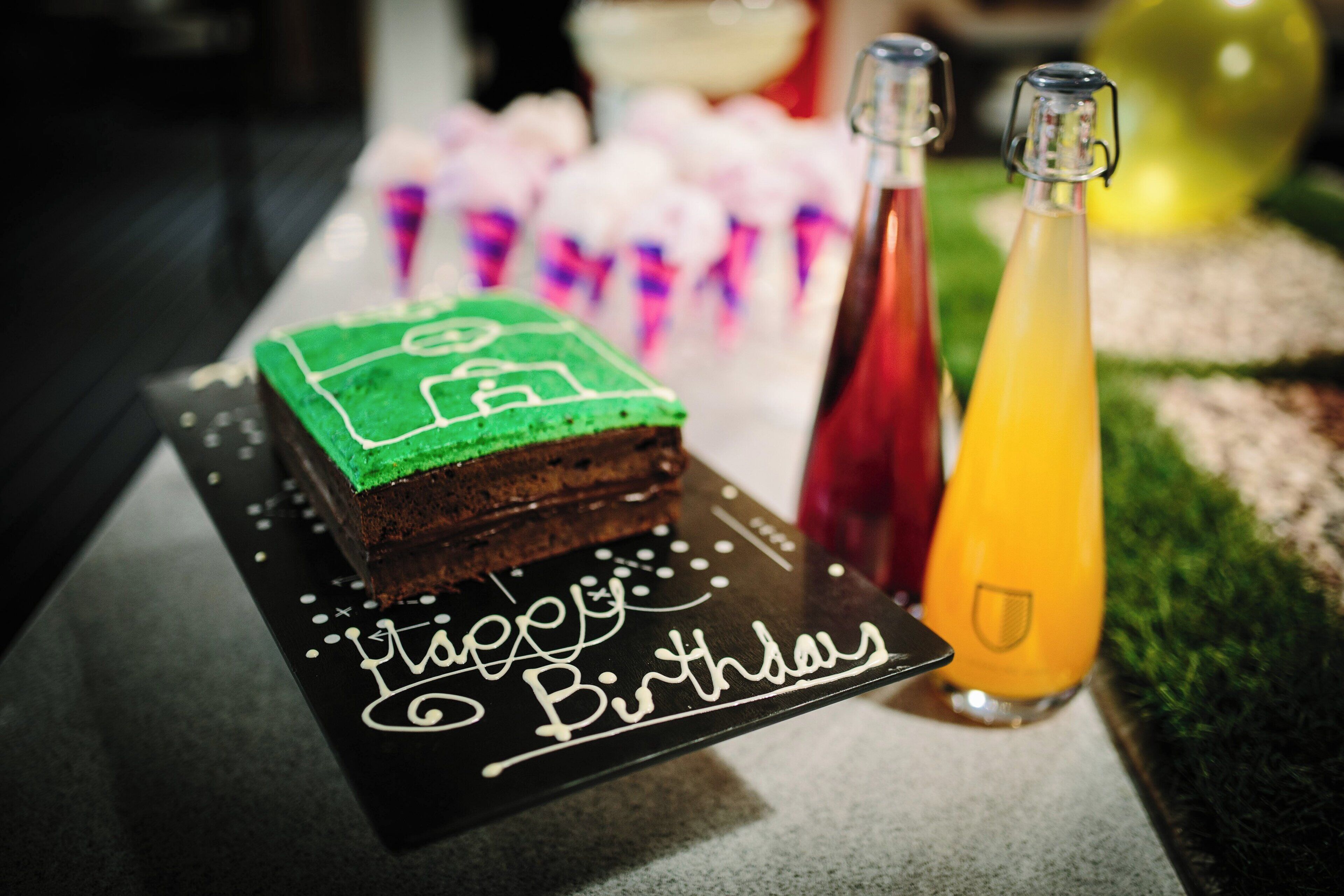 A birthday cake with a soccer field design on a black tray with "Happy Birthday" written on it.