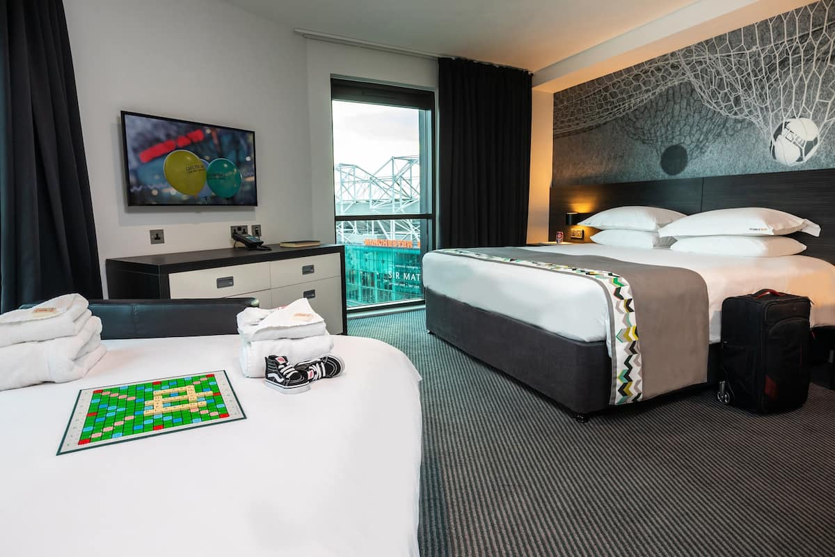 A hotel room with a large bed, a desk, a chair, a window with a view of a bridge, and a wall with a soccer ball design.
