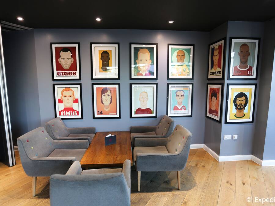 A conference room with a wooden table and grey upholstered chairs, framed posters on the wall, and wooden flooring.