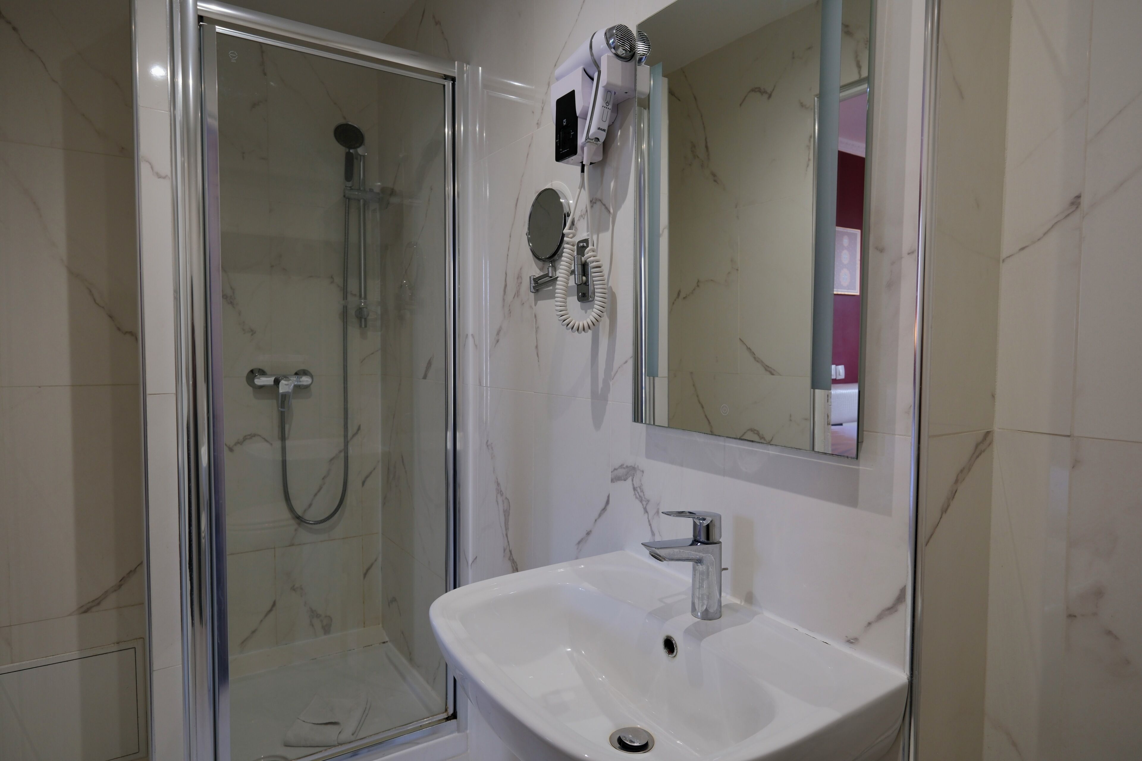 Un baño con ducha de vidrio, lavamanos blanco y secador de pelo montado en la pared.