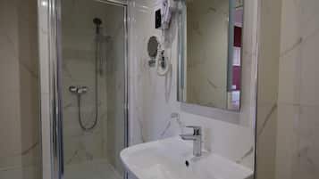 Un baño con ducha de vidrio, lavamanos blanco y secador de pelo montado en la pared.