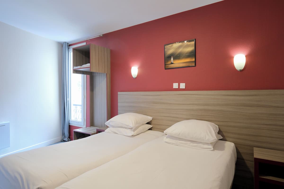 A hotel room with two beds, a red wall, and a window with curtains.