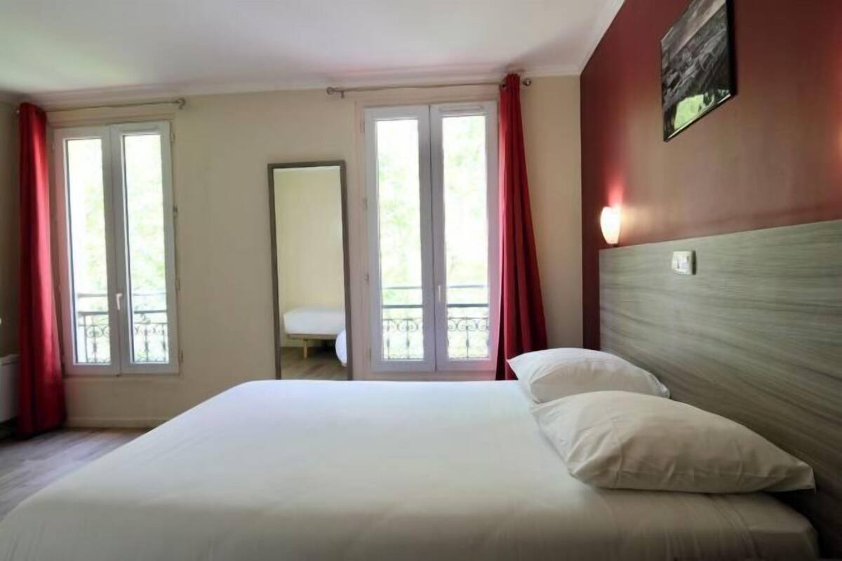 A hotel room with a bed, a nightstand, a mirror, and a window with curtains.