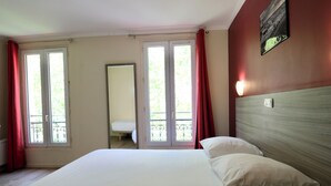 A hotel room with a bed, a window with curtains, a door, and a wall-mounted light. - Hipotel Paris Gambetta Republique (Paris)