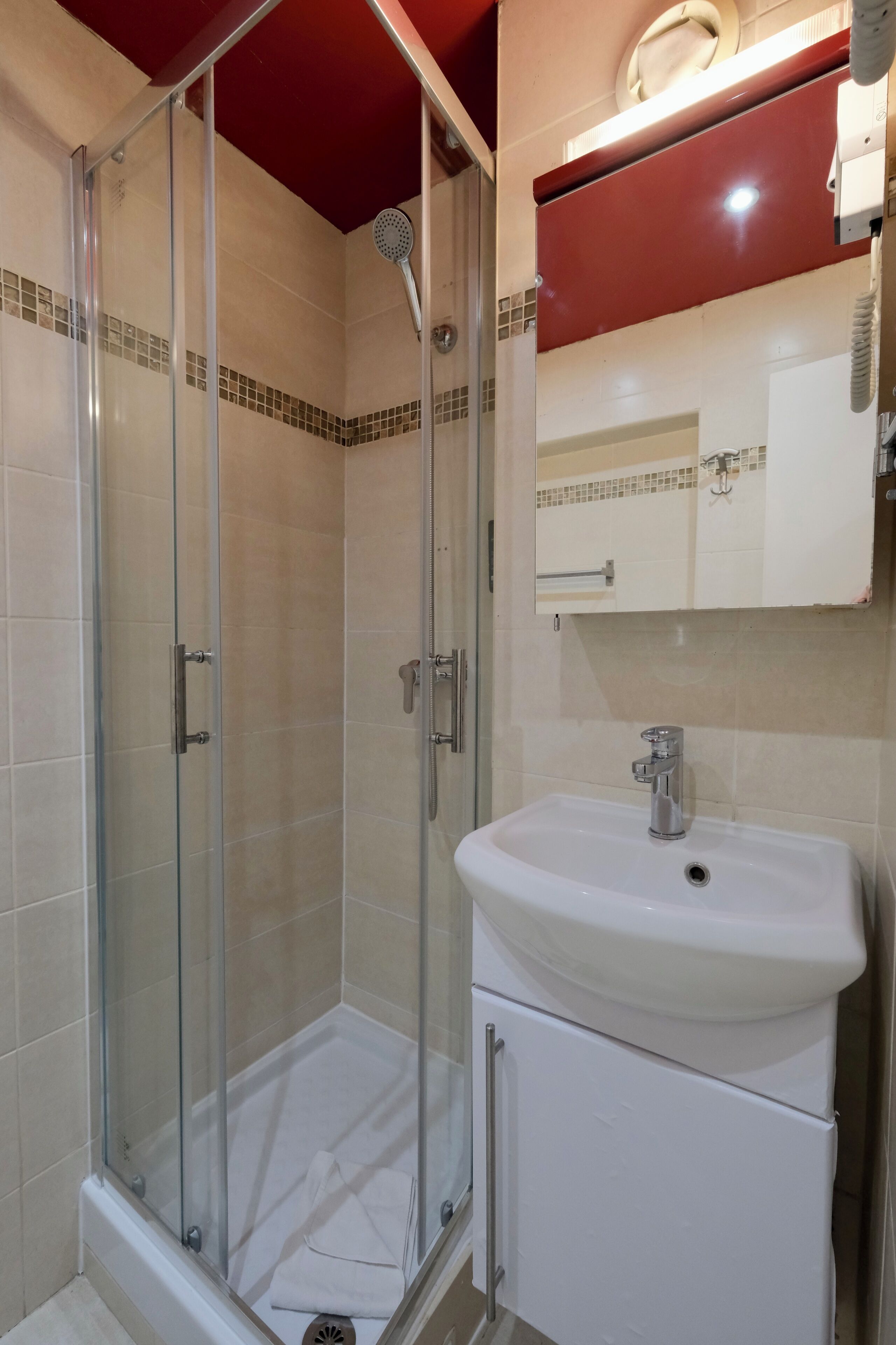 A shower with a glass door, a white sink, and a red ceiling.