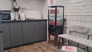 A modern kitchen with a microwave, coffee maker, and refrigerator. There is a bench and a glass table with magazines. - Hipotel Paris Gambetta Republique (Paris)