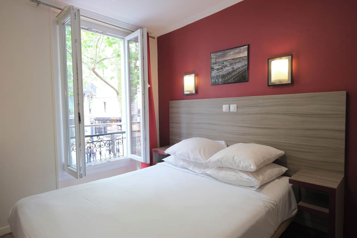 A hotel room with a bed, a window with a view, and two wall-mounted lights.