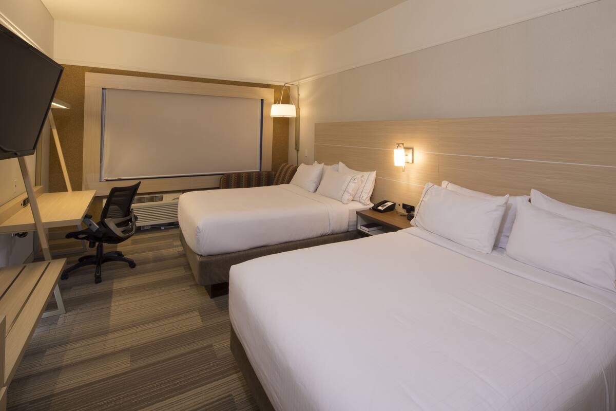 A hotel room with two beds, a desk, a chair, a TV, and a projector screen.
