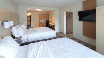 A hotel room with two beds, a television, a desk with a chair, a kitchenette, and a bathroom.