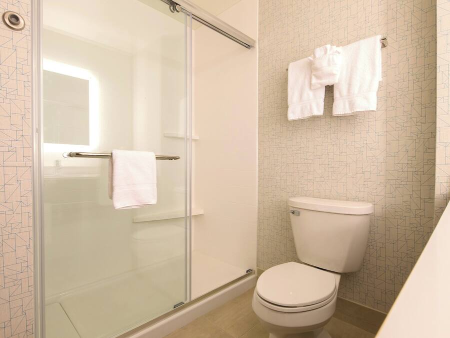 Ein Badezimmer mit Duschkabine aus Glas, Toilette und Handtuchhalter mit Handtüchern.