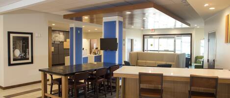 A modern hotel lobby with a reception desk, seating area, and a large window providing natural light.