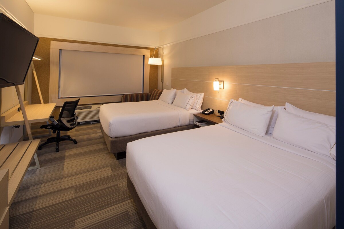 Een hotelkamer met twee bedden, een bureau met stoel, een televisie en een groot raam.