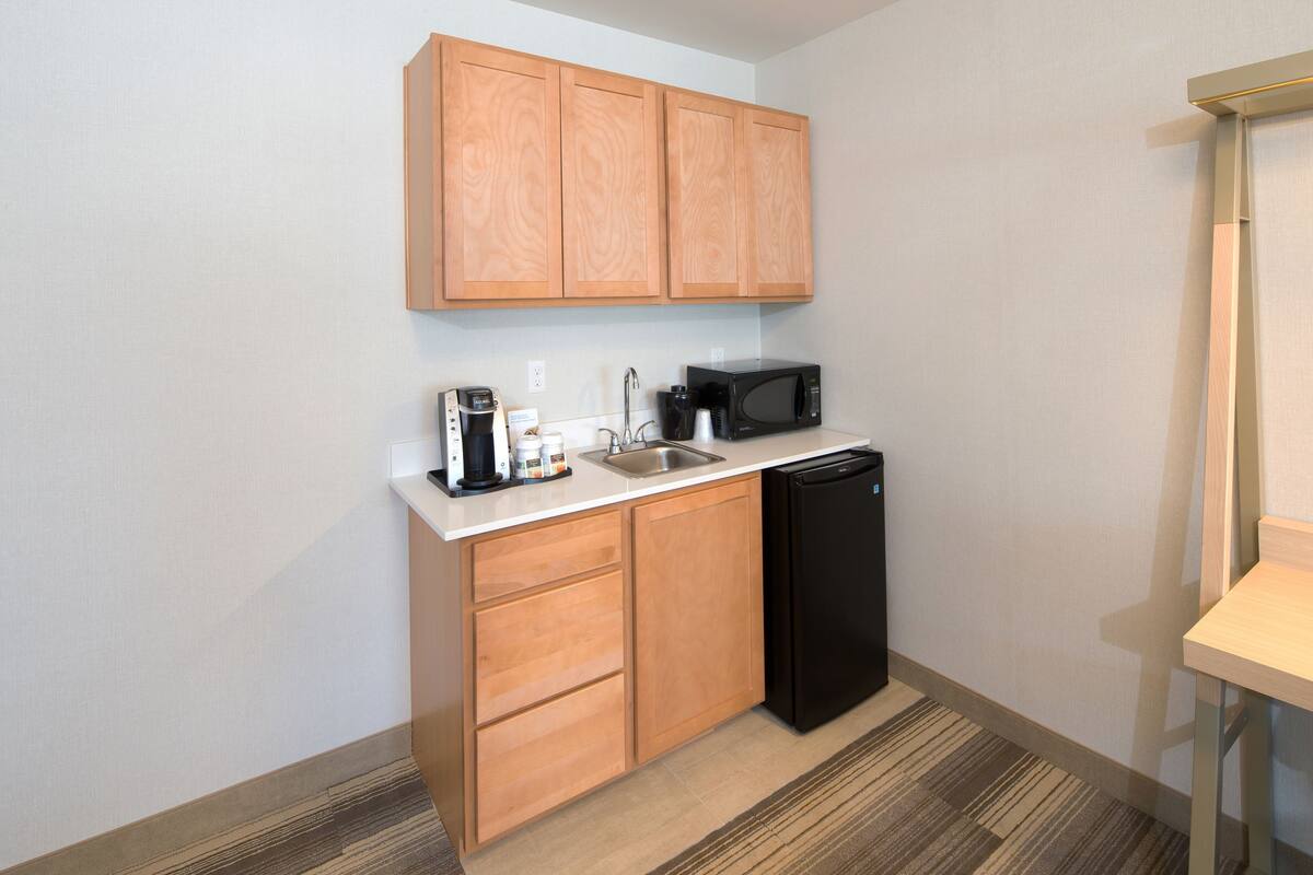 A compact kitchen with wooden cabinets, a black microwave, a coffee maker, and a dishwasher.