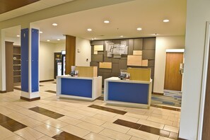 A hotel reception area with two reception desks, a digital screen, and a wall-mounted sign. - Holiday Inn Express & Suites Rochester Hill - Detroit Area by IHG (Rochester)