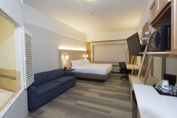 Een hotelkamer met een bed, een bank, een bureau met een computer, een televisie en een magnetron.