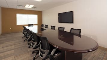 A conference room with a long table, multiple chairs, a flat-screen TV, and a large window.