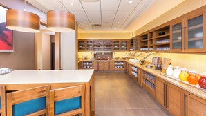 A modern kitchen with wooden cabinets, a central island with chairs, and a breakfast bar. - Hyatt Place Canton (North Canton)