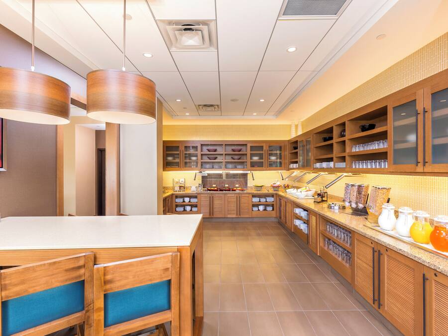 A modern kitchen with wooden cabinets, a central island with chairs, and a breakfast bar.